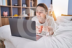 Young caucasian woman using laptop drinking coffee at bedroom