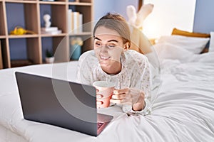 Young caucasian woman using laptop drinking coffee at bedroom