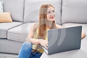 Young caucasian woman using laptop sitting on floor at home