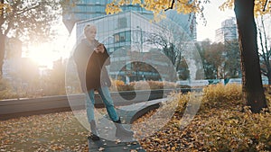 Young caucasian woman using phone in the city park in front of office building in autumn