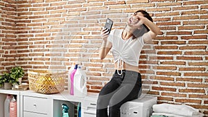 Young caucasian woman using smartphone waiting for washing machine with winner expression at laundry room