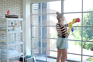 Young Caucasian woman Wear yellow rubber gloves is holding Cleanser bottle and sponge. She is cleaning and wiping the glass window