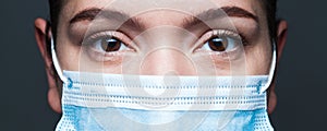 Young caucasian woman wearing blue surgical face mask closeup wide screen portrait