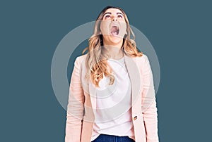 Young caucasian woman wearing business clothes angry and mad screaming frustrated and furious, shouting with anger