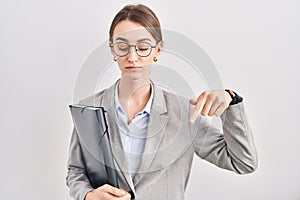 Young caucasian woman wearing business clothes and glasses pointing down looking sad and upset, indicating direction with fingers,