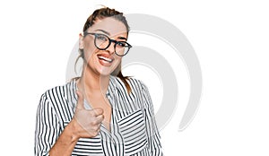 Young caucasian woman wearing business shirt and glasses doing happy thumbs up gesture with hand