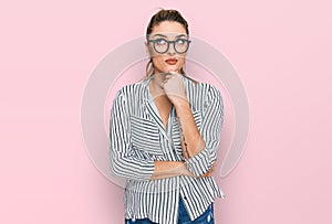 Young caucasian woman wearing business shirt and glasses with hand on chin thinking about question, pensive expression