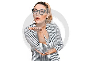 Young caucasian woman wearing business shirt and glasses looking at the camera blowing a kiss with hand on air being lovely and