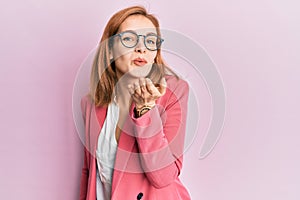 Young caucasian woman wearing business style and glasses looking at the camera blowing a kiss with hand on air being lovely and