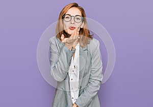 Young caucasian woman wearing business style and glasses looking at the camera blowing a kiss with hand on air being lovely and