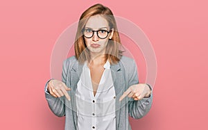 Young caucasian woman wearing business style and glasses pointing down looking sad and upset, indicating direction with fingers,