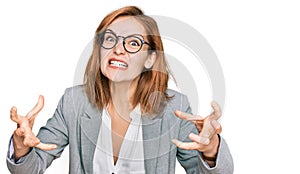 Young caucasian woman wearing business style and glasses shouting frustrated with rage, hands trying to strangle, yelling mad photo