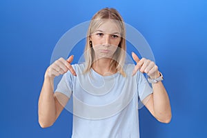 Young caucasian woman wearing casual blue t shirt pointing down looking sad and upset, indicating direction with fingers, unhappy