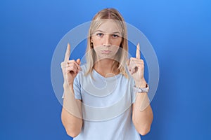 Young caucasian woman wearing casual blue t shirt pointing up looking sad and upset, indicating direction with fingers, unhappy