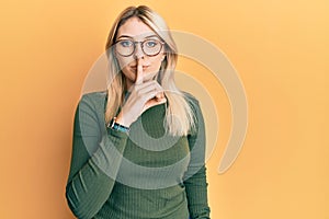 Young caucasian woman wearing casual clothes and glasses asking to be quiet with finger on lips