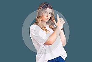 Young caucasian woman wearing casual clothes holding symbolic gun with hand gesture, playing killing shooting weapons, angry face