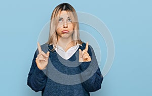 Young caucasian woman wearing casual clothes pointing up looking sad and upset, indicating direction with fingers, unhappy and