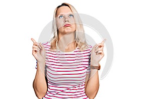 Young caucasian woman wearing casual clothes pointing up looking sad and upset, indicating direction with fingers, unhappy and