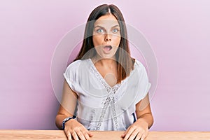 Young caucasian woman wearing casual clothes sitting on the table scared and amazed with open mouth for surprise, disbelief face