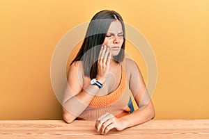 Young caucasian woman wearing casual clothes sitting on the table touching mouth with hand with painful expression because of