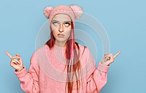 Young caucasian woman wearing casual clothes and wool cap pointing up looking sad and upset, indicating direction with fingers,
