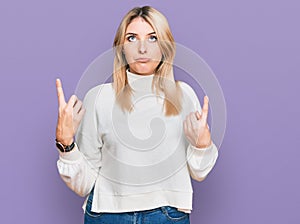 Young caucasian woman wearing casual winter sweater pointing up looking sad and upset, indicating direction with fingers, unhappy