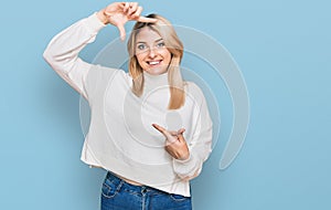 Young caucasian woman wearing casual winter sweater smiling making frame with hands and fingers with happy face