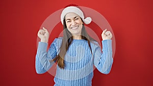 Young caucasian woman wearing christmas hat with arms raised up over isolated red background