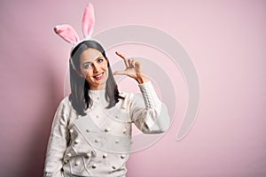 Young caucasian woman wearing cute easter rabbit ears over pink isolated background smiling and confident gesturing with hand