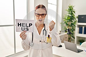 Young caucasian woman wearing doctor uniform holding help us banner annoyed and frustrated shouting with anger, yelling crazy with