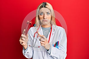 Young caucasian woman wearing doctor uniform holding tuning fork depressed and worry for distress, crying angry and afraid