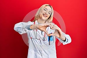 Young caucasian woman wearing doctor uniform and stethoscope smiling in love doing heart symbol shape with hands