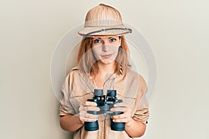 Young caucasian woman wearing explorer hat looking through binoculars skeptic and nervous, frowning upset because of problem