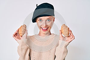 Young caucasian woman wearing french look with beret holding croissants smiling and laughing hard out loud because funny crazy