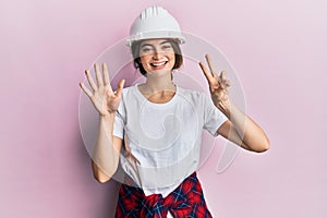 Young caucasian woman wearing hardhat showing and pointing up with fingers number seven while smiling confident and happy