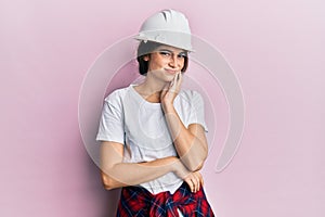 Young caucasian woman wearing hardhat touching mouth with hand with painful expression because of toothache or dental illness on