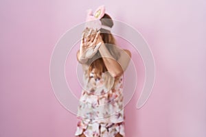 Young caucasian woman wearing sleep mask and pajama covering eyes with hands and doing stop gesture with sad and fear expression