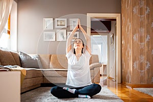 Young Caucasian woman wearing sports clothes sits on floor in living room and does yoga. Home fitness and relax