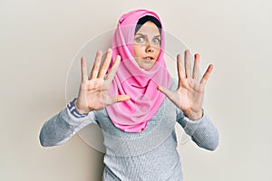 Young caucasian woman wearing traditional islamic hijab scarf afraid and terrified with fear expression stop gesture with hands,