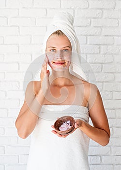 Young caucasian woman wearing white towels applying scrub on her face
