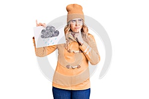 Young caucasian woman wearing winter clothes holding rain draw serious face thinking about question with hand on chin, thoughtful