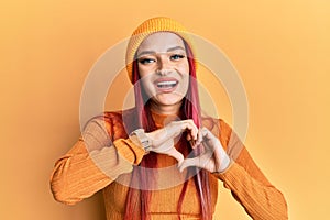 Young caucasian woman wearing wool cap smiling in love showing heart symbol and shape with hands