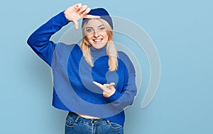 Young caucasian woman wearing wool winter sweater and cap smiling making frame with hands and fingers with happy face