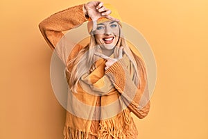 Young caucasian woman wearing wool winter sweater and cap smiling making frame with hands and fingers with happy face