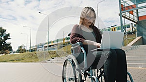 Young caucasian woman in the wheelchair using laptop. Train passing in the background