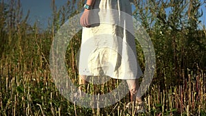 A young caucasian woman in white dress walks in a summer meadow touching grass in slowmo