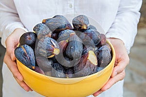 Young caucasian woman in white linen cotton shirt holds in hands yellow ceramic bowl with freshly picked ripe organic purple figs photo