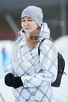 Young Caucasian woman in a winter jacket with black backpack walks at wintry weather
