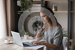 Young Caucasian woman work on laptop talking on cellphone