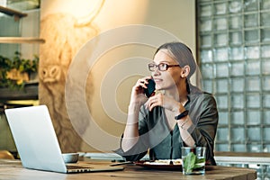 Young caucasian woman working at her desk with laptop and talking on phone